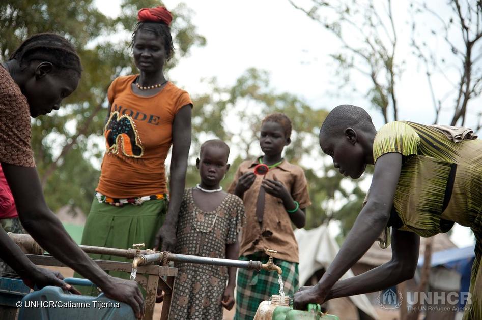 Nyawon (right), 28 and a foster mom, fills her water jugs at the communal pump nearby her temporary home at the Tierkidi Refugee Camp on 21 November 2014. ; Nyawon has taken in five abandoned children that fled the civil war South Sudan to this refugee camp in Tierkidi, Ethiopia, while she searches in vain through friends of friends contacts for her own three children that she hopes are in other camps in Uganda or Kenya. "I miss my phone. I had one in South Sudan but I sold everything I had to get here. If I had a phone, I could call and see if my children were alive. I go to collect firewood to sell and with the money I make [$2.50 every three weeks], I buy a phone card. I have to beg to use people's phones and some won't lend it, others hurry me and the line cuts or the money runs out without me getting anywhere. If I had one, I could take my time. I miss my job at home as it meant I could buy my children everything. I can't buy these children anything. We just have the clothes on our bodies. These children don't know where their parents are. I try to comfort them with the hope that they will find their parents again like I will my children."