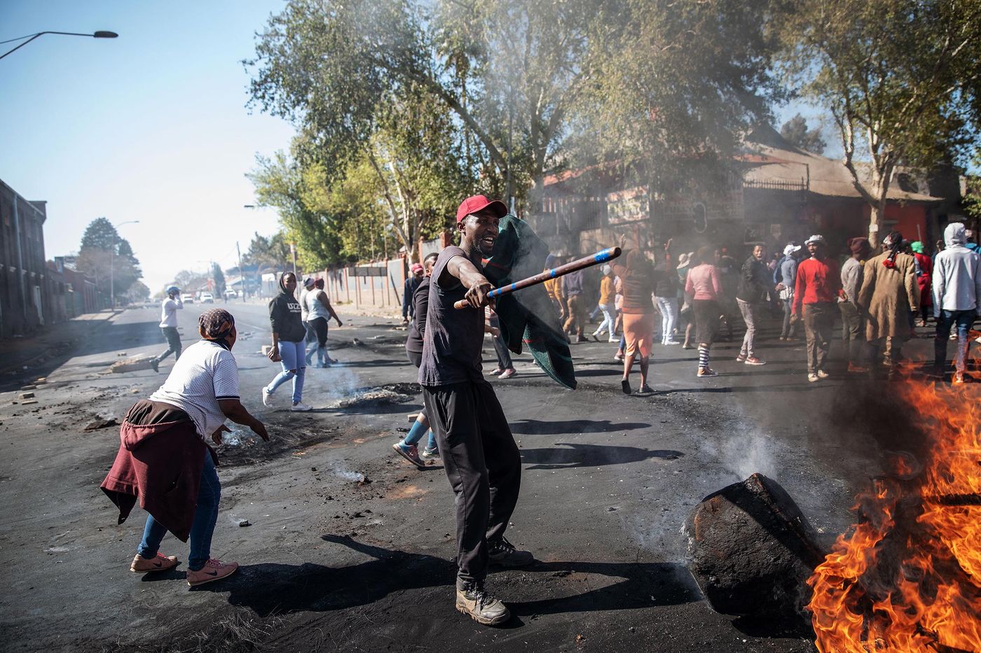 A man holds a stick in front of burning furniture in the streets during riots in Johannesburg, SA.  
Credit: Getty Images