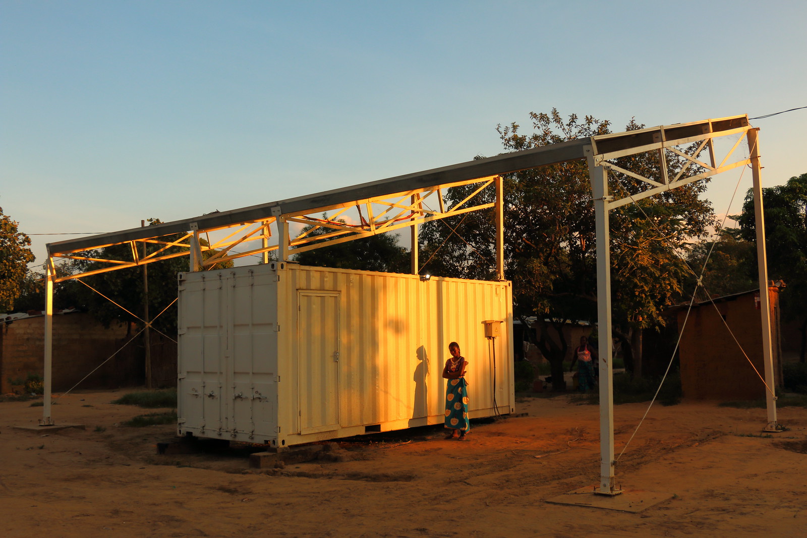 Woman in rural Tanzania standing next to a solar home system