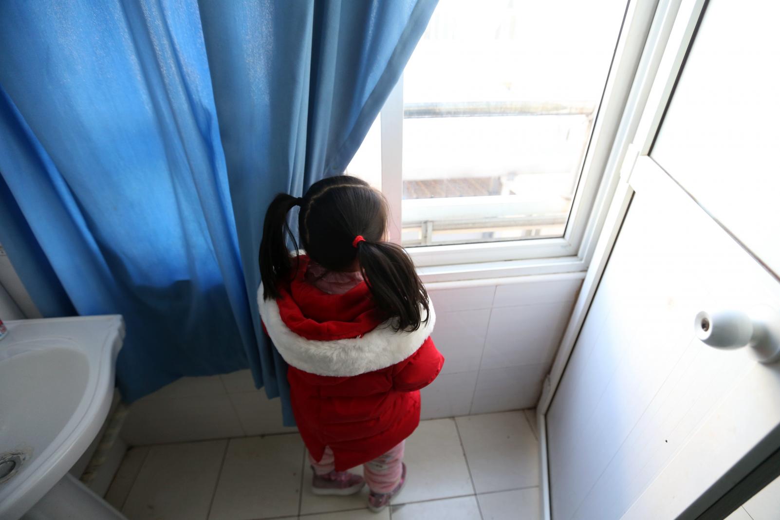 A child looking out the window, unable to go outside to play.