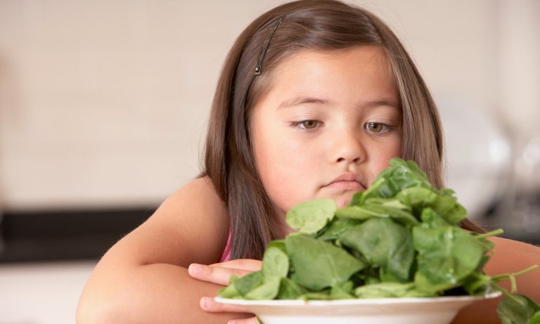 Child looking at a plate of spinach. 