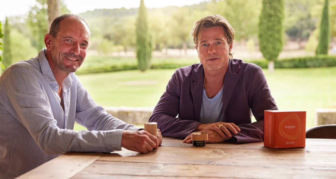 [Image description: Brad Pitt sitting at a table in a green field.] Via le-domaine-skincare.myshopify.com]