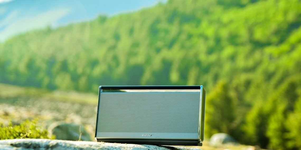 A portable speaker sitting on a rock, under sunlight.