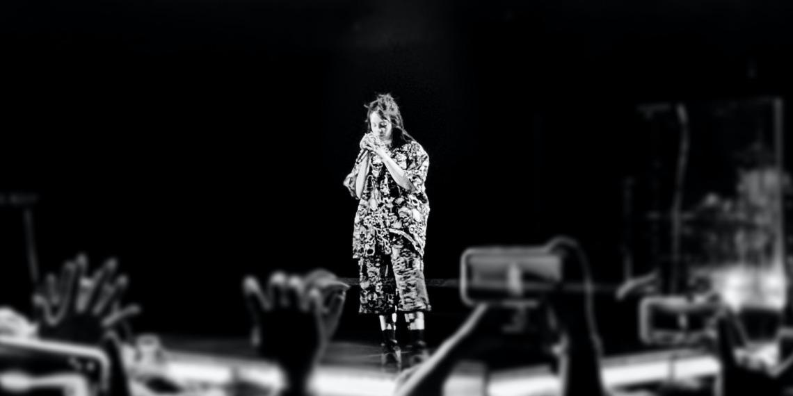 Billie Eilish at a concert, seen from afar.