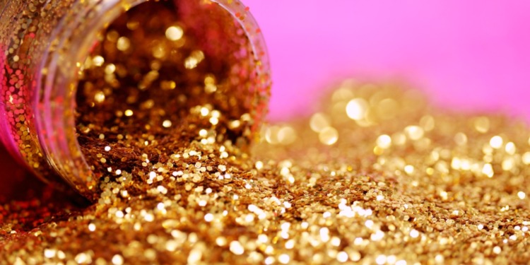 gold glitter spilled from a bottle into a pink background.
