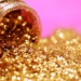 gold glitter spilled from a bottle into a pink background.