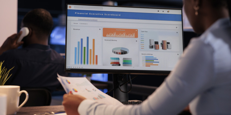 Office employee analyzing business charts on computer and documents, looking at online research data to create presentation. Working with information on report, statistics on pc.