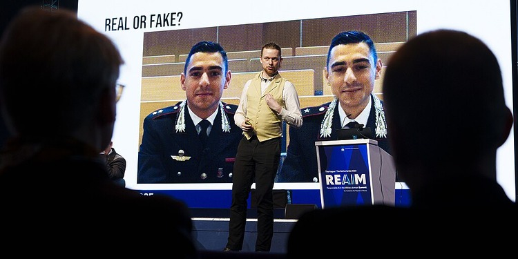 REAIM speaker stands in front of an image that reads "Real or fake?"