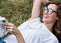 A woman laying down on the grass wearing Eco-Friendly Glasses while reading a book.