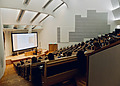 A university room with the students in a theatre like setup with a professor explaining a course using a projector.