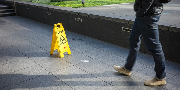 A man walks toward a yellow caution sign to prevent slip and fall accidents