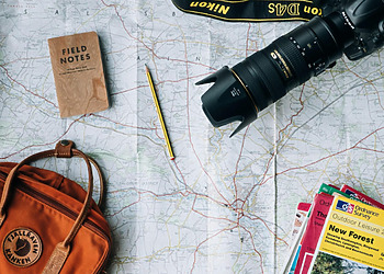 Map with a camera and orange travel bag on top of it.