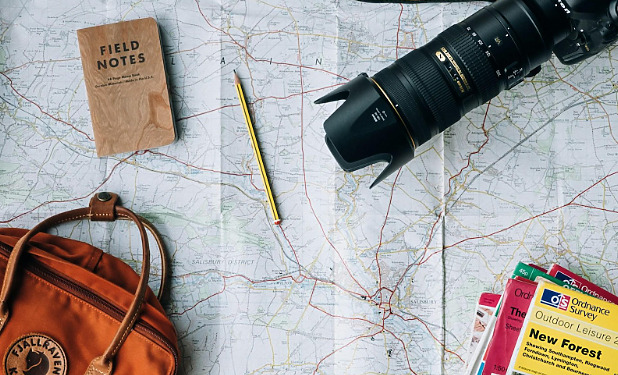 Map with a camera and orange travel bag on top of it.