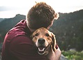 Men hugging his golden retriever while sitting on the floor, a the top of a hill overlooking a green valley.
