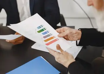 An insurance advisor handing a printed color financial performance bar chart report to a customer during a meeting.
