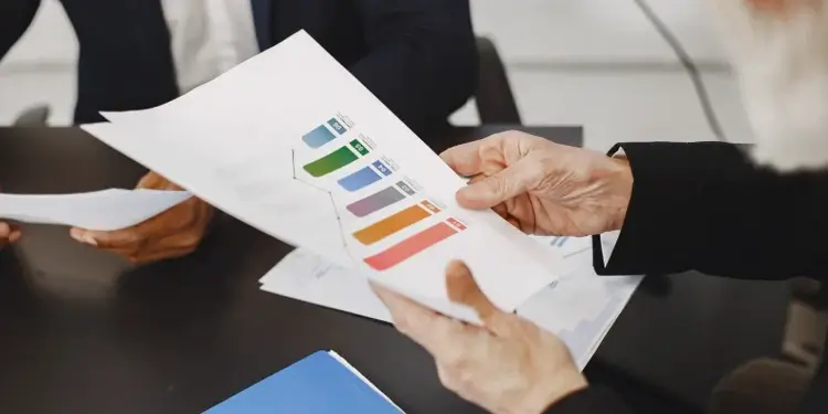 An insurance advisor handing a printed color financial performance bar chart report to a customer during a meeting.