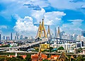 Bhumibol Bridge spanning the Chao Phraya River with the Bangkok city skyline and highway traffic under a blue sky.