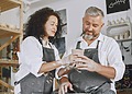 A smiling middle-aged small business owner couple working together on a handmade clay pottery pot in their studio shop.