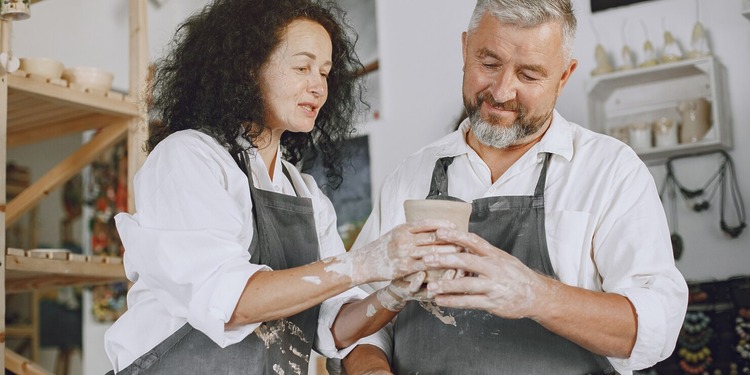 A smiling middle-aged small business owner couple working together on a handmade clay pottery pot in their studio shop.