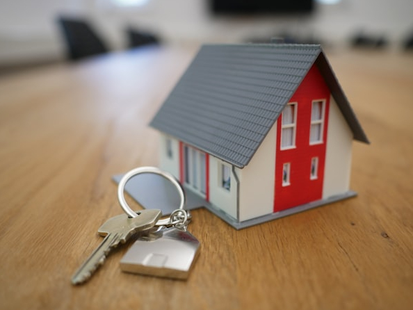 Small model home next to a key chain with house keys. On a table.