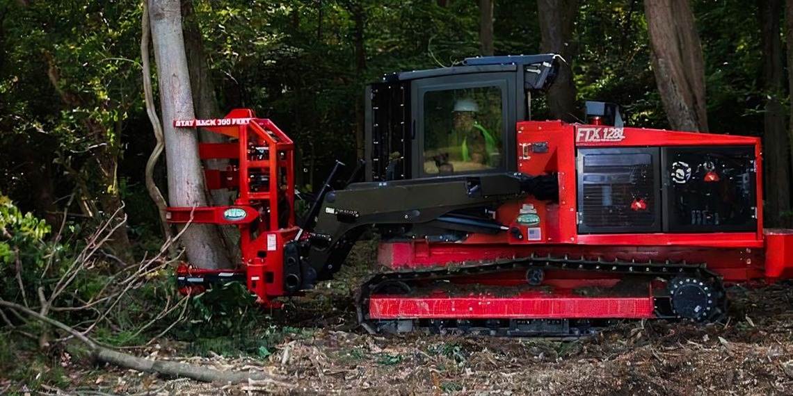 A red tracked forestry tractor using a hydraulic tree shear attachment to selectively cut a tree trunk in dense woods.