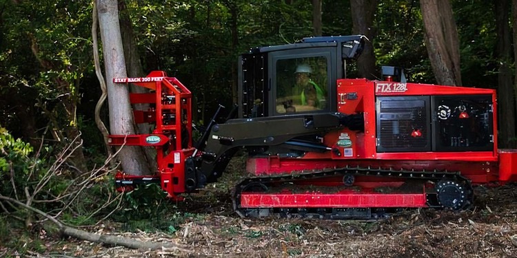 A red tracked forestry tractor using a hydraulic tree shear attachment to selectively cut a tree trunk in dense woods.