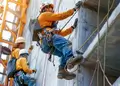 Construction workers equipped with safety harnesses and hard hats performing maintenance on a building
