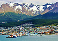 Colorful houses along the waterfront of Ushuaia with snow-capped Martial Mountains rising in the background beneath a blue sky.