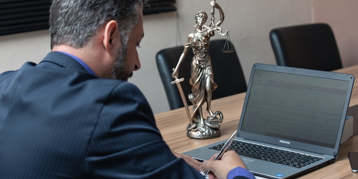 A smartphone lying on a wooden desk next to a classic judge's gavel and a legal scale of justice.