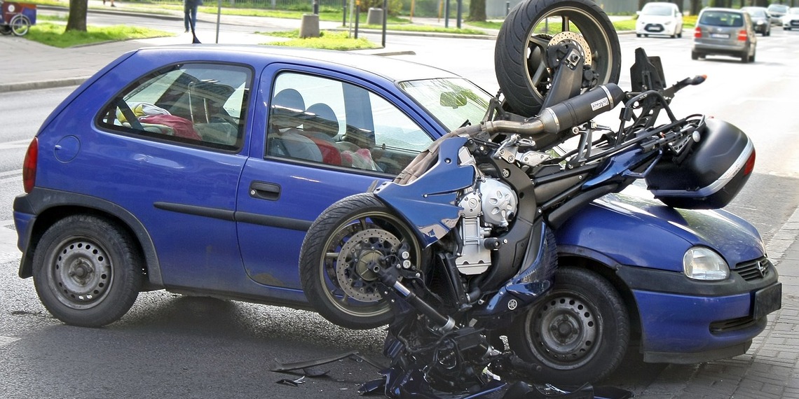 A silver passenger car with severe front-end damage from a vehicle collision parked on the side of a road.