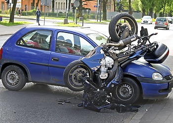 A silver passenger car with severe front-end damage from a vehicle collision parked on the side of a road.