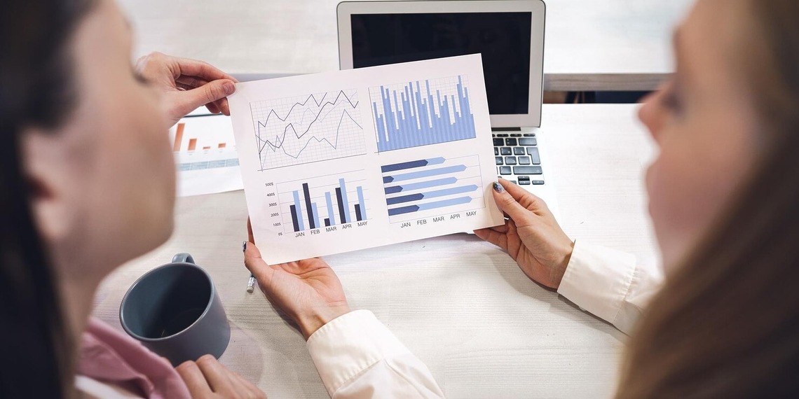 Two business professionals passing a colorful financial growth bar chart report over a desk.