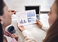 Two business professionals passing a colorful financial growth bar chart report over a desk.