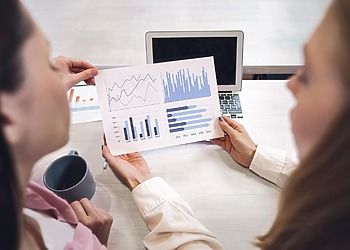 Two business professionals passing a colorful financial growth bar chart report over a desk.