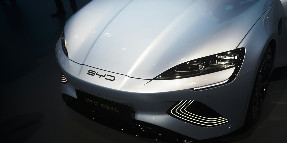 A sleek, modern white BYD electric sedan charging at a high-speed urban power station under clear skies.