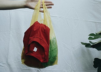 A hand holds a yellow plastic bag containing clothe