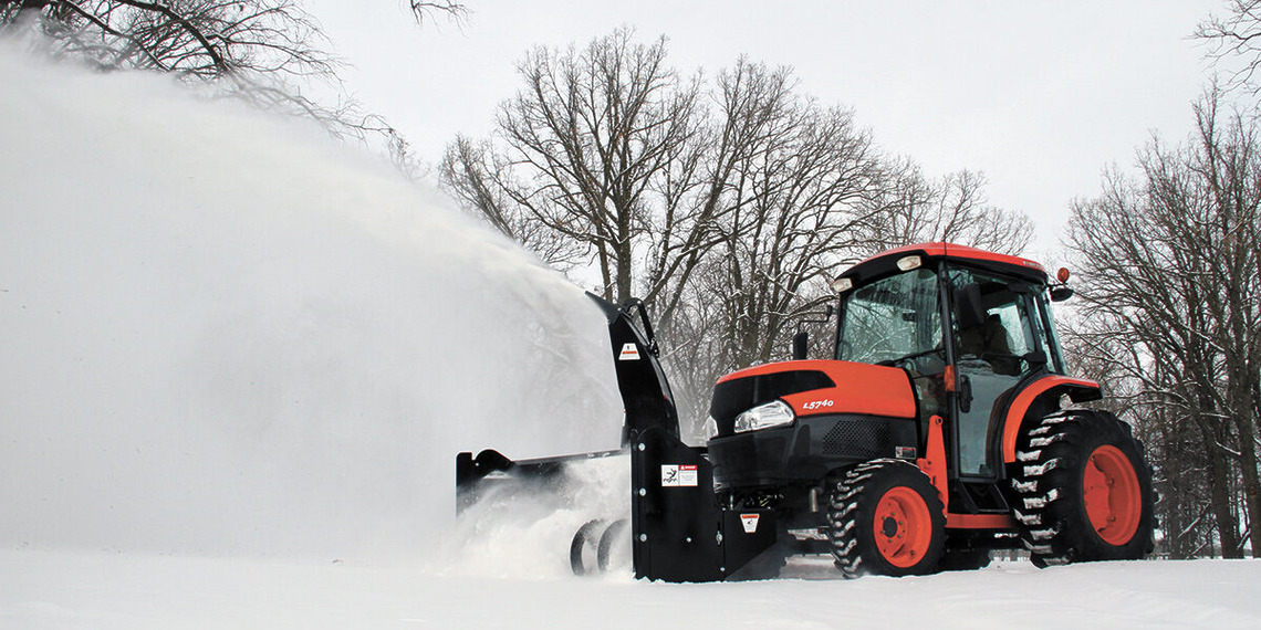 An orange Kubota utility tractor operating an Erskine front-mount snowblower attachment to clear deep snow from a rural driveway.
