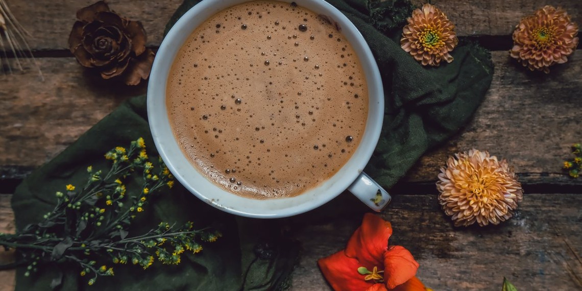 A cappuccino cup surrounded by vibrant flowers on a rustic wooden table.