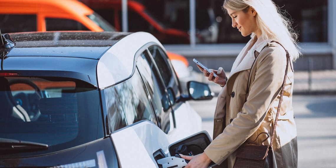 Traveler charging an electric rental car at a public charging station during a sustainable road trip.