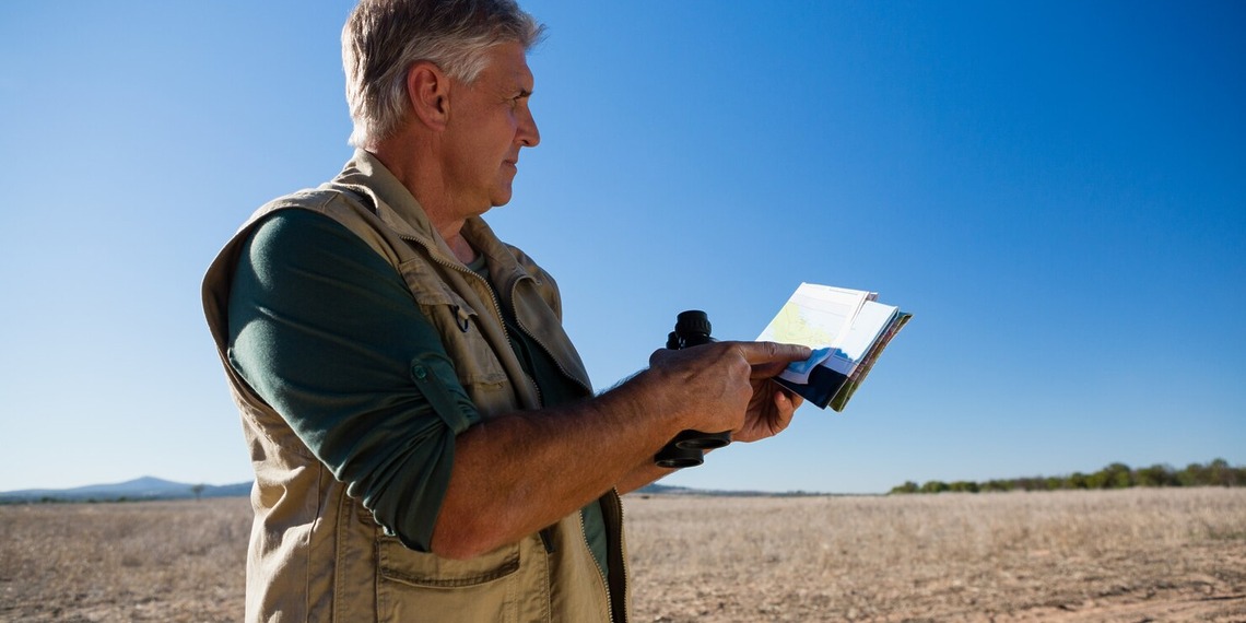 Environmental consultant conducting a field assessment in a dry landscape while reviewing site data and environmental conditions.