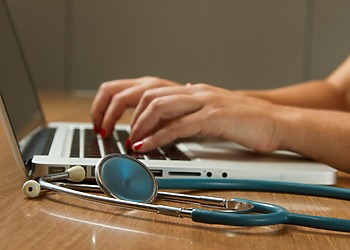 person sitting while using laptop computer and green stethoscope near