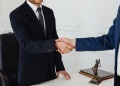 Two men in suits shaking hands in a formal legal office environment symbolizing an agreement.