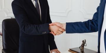 Two men in suits shaking hands in a formal legal office environment symbolizing an agreement.