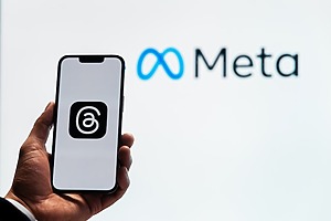 A phone with the Threads logo is held in front of a Meta sign.