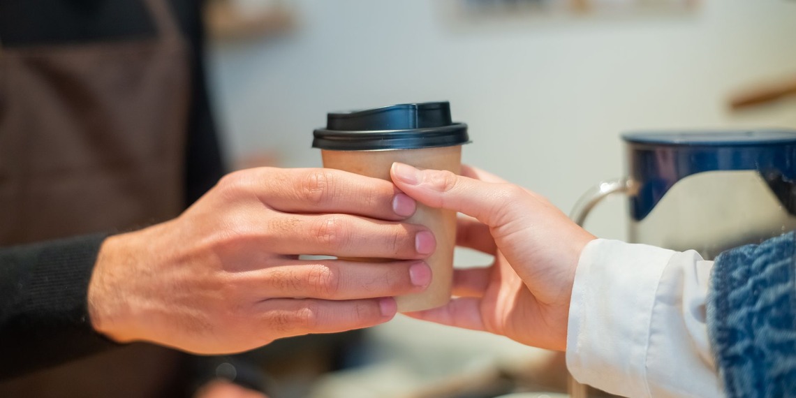 Close-up of barista handing a to-go coffee cup to a customer in a cozy cafe.