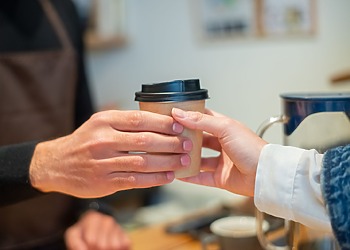 Close-up of barista handing a to-go coffee cup to a customer in a cozy cafe.