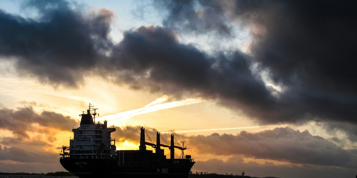 Cargo ship sailing under dark clouds at sunset