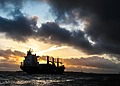 Cargo ship sailing under dark clouds at sunset