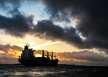 Cargo ship sailing under dark clouds at sunset