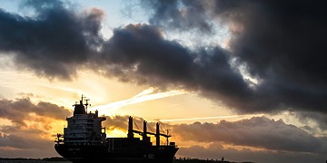 Cargo ship sailing under dark clouds at sunset
